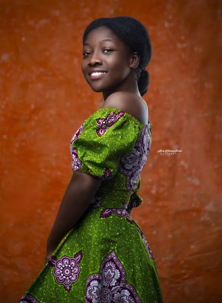 Emmy Mawumenyo in a green and purple print dress, smiling over her shoulder.
