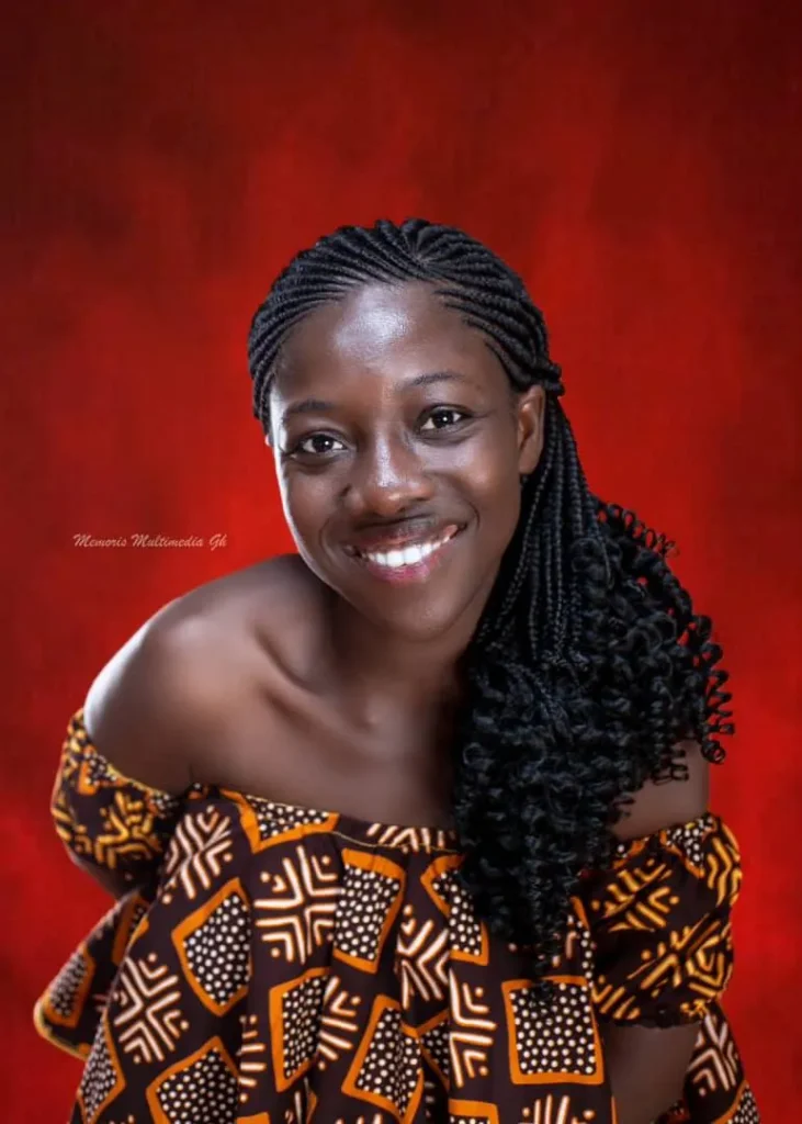 Emmy Mawumenyo smiling, in an off shoulder African print top against a red backdrop.